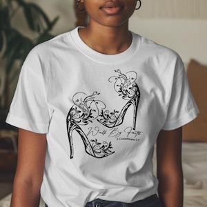 May include: White t-shirt with a black graphic of two high-heeled shoes with floral designs. The text "Walk By Faith" and "2 Corinthians 5:7" is printed below the shoes.