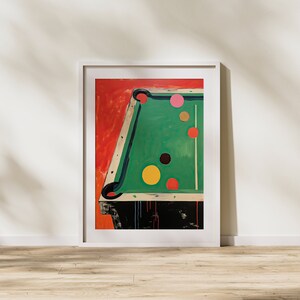 May include: A framed painting depicting a green pool table with colourful balls. The table is set against a red background. The balls are arranged in a line, with the cue ball at the front.