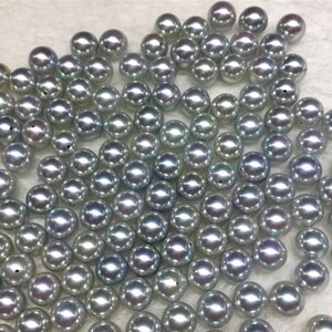 Puede incluir: Un conjunto de perlas grises y brillantes dispersas sobre una superficie. Las perlas tienen una superficie lisa y reflectante, con sutiles variaciones de color y tama&ntilde;o. El efecto general es de elegancia y belleza natural, adecuado para la creaci&oacute;n de joyas.