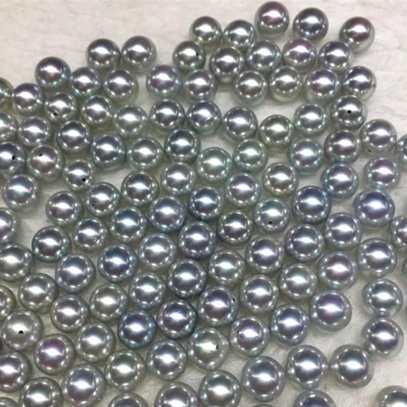 Puede incluir: Un conjunto de perlas grises y brillantes dispersas sobre una superficie. Las perlas tienen una superficie lisa y reflectante, con sutiles variaciones de color y tama&ntilde;o. El efecto general es de elegancia y belleza natural, adecuado para la creaci&oacute;n de joyas.