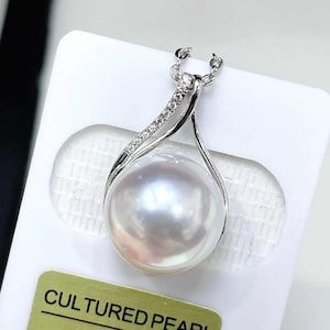 May include: A silver-toned pendant necklace featuring a large, round, white cultured pearl suspended from a curved metal bail. The bail is accented with a row of small, clear, sparkling stones and connects to a delicate silver-toned chain.
