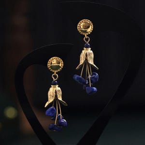 Peut inclure: Boucles d'oreilles en or avec un design en forme de cloche et des accents de pierres précieuses bleues.