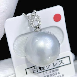 May include: A large, round, white South Sea pearl pendant suspended from a silver-toned bail encrusted with small clear stones. The pendant is mounted on a white display card featuring the Japanese text 白蝶クレス and the measurement 17.2mm.