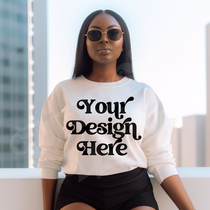 May include: Cream-colored sweatshirt with the text "Your Design Here" in a bold, black, retro font. The long-sleeved top is paired with black shorts. The model is wearing gold-rimmed sunglasses.