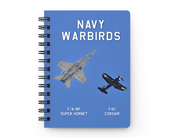 May include: A blue notebook with a spiral binding features a photo of two Navy fighter jets. The text "NAVY WARBIRDS" is at the top of the notebook. The top jet is an F/A-18F Super Hornet and the bottom jet is an F4U Corsair.