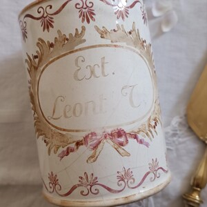Peut inclure: Pot en céramique blanche avec un motif floral rouge et or. Le pot porte une étiquette sur laquelle est inscrit "Ext. Leont. C".