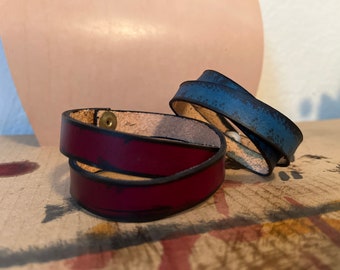 Può includere: Due braccialetti in pelle, uno color borgogna con cuciture nere e un bottone in ottone, l'altro blu con una finitura invecchiata.