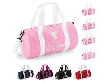 Peut inclure: Sac de sport rose avec des poignées blanches et une bandoulière blanche. Le sac présente un motif de ballerine et le nom "Evelyn" en blanc. D'autres sacs de différentes couleurs sont également présentés.