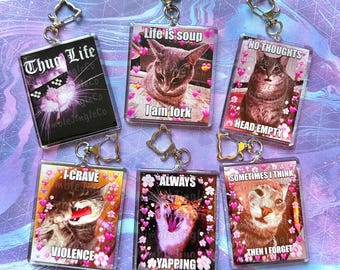 May include: A collection of acrylic keychains featuring cat images with humorous text. The keychains have silver-colored hardware and include phrases like "Thug Life," "Life is soup I am fork," and "No thoughts head empty."