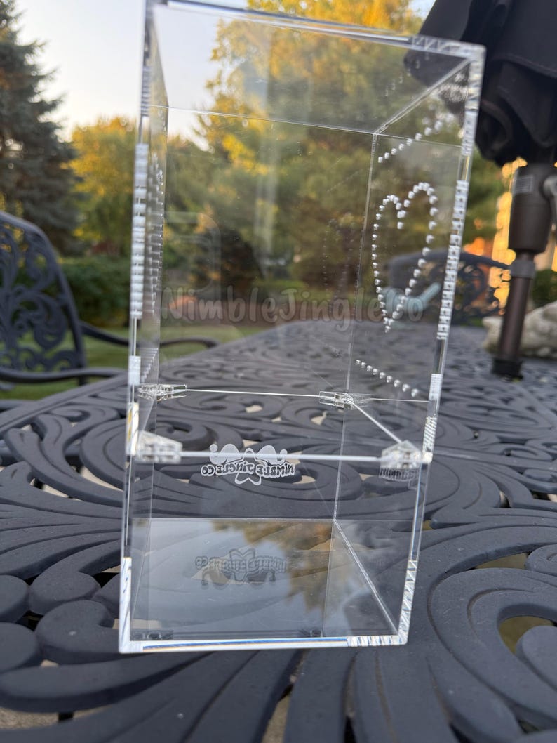 May include: A clear acrylic box with a heart design made of small dots. The box has the text "NimbleJingleCo" on the side and bottom. The box is on a dark, patterned surface.