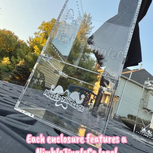 May include: Clear acrylic display case with a NimbleJingleCo logo. The case is angled, showing the interior and exterior details. The text "Each enclosure features a NimbleJingleCo logo!" is displayed in pink.