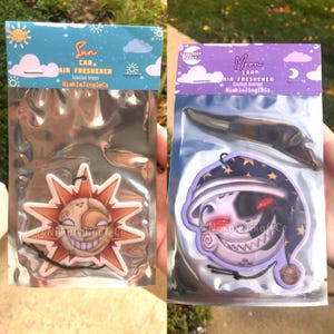 May include: Two car air fresheners, one with a sun design and the text "Sun Car Air Freshener Scented Lemon NimbleJingleCo" and the other with a moon design and the text "Moon Car Air Freshener Scented Lavender NimbleJingleCo."