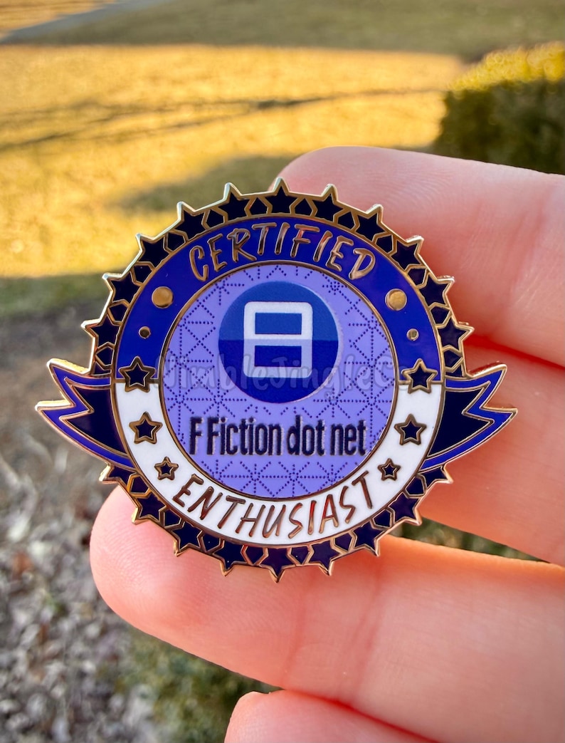 Op de afbeelding: Een ronde emaille pin in blauw en goud met de tekst "CERTIFIED ENTHUSIAST" en "F Fiction dot net". De pin heeft een sterrenpatroonrand en een centrale blauwe cirkel met een wit symbool.