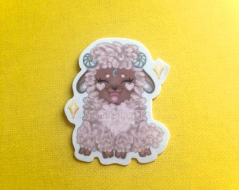 May include: A pink and brown cartoon sheep sticker with a crescent moon on its forehead and sparkling accents. The sheep is smiling with its tongue sticking out.