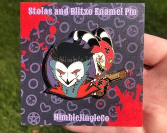 Peut inclure: Épinglette en émail Stolas et Blitzo représentant un démon rouge et noir avec des cornes et un démon violet et bleu avec un pistolet. L'épingle est sur une carte avec un fond rouge et noir et le texte "Stolas and Blitzo Enamel Pin" et "NimbleJingleCo".