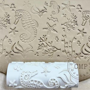 May include: A white rolling pin with a seahorse, starfish, and seaweed design. The rolling pin is used to create decorative patterns in clay or dough.