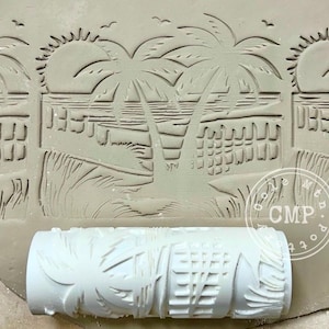 May include: A white roller with a tropical beach design is shown next to a clay impression. The design includes palm trees, a sunset, and a shoreline. The roller is cylindrical and features a repeating pattern.