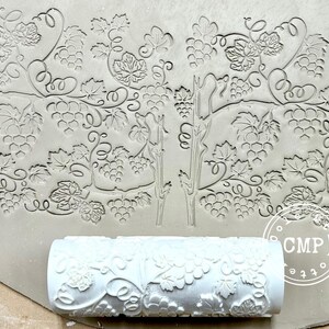 May include: A light gray clay slab with a grape vine pattern and a white roller with the same design. The roller is used to imprint the grape vine pattern onto the clay. The design includes grapes, leaves, and vines.