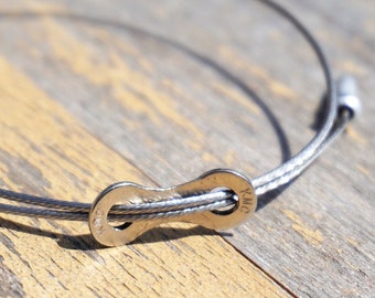 Pode incluir: Uma pulseira de prata com um fecho de elo de corrente de bicicleta. A pulseira é feita de duas fitas de cabo de prata fino.