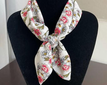 May include: A white floral patterned scarf with pink and green flowers tied around a black mannequin neck.