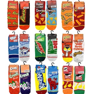 May include: Twelve pairs of colorful socks featuring various popular food and beverage brands. The socks are arranged in four rows of three pairs each. The brands featured include Reese's, Doritos, Cheetos, Hawaiian Punch, Mountain Dew, Kool-Aid, and Pringles.