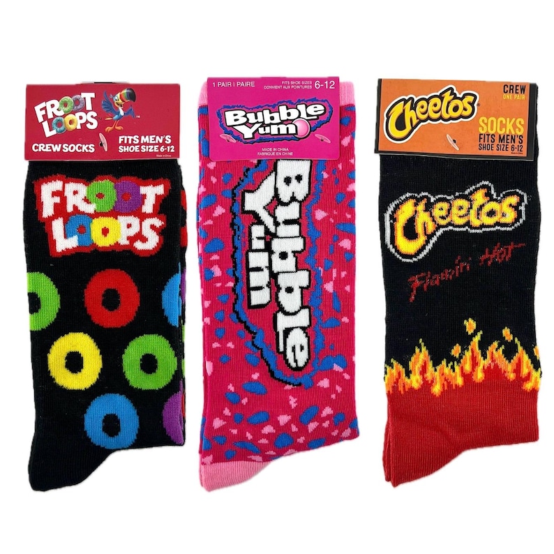 May include: Three pairs of men's crew socks featuring colorful designs of popular snack foods. The socks are black with a Froot Loops design, pink with a Bubble Yum design, and black with a Cheetos design.