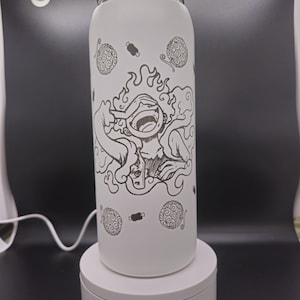 May include: White stainless steel water bottle with a black and white graphic of a cartoon character with flames and a swirl design. The character is surrounded by several black and white swirl designs.