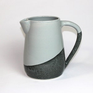 May include: A grey and black ceramic jug with a speckled black glaze on the bottom half. The jug has a rounded body and a handle.