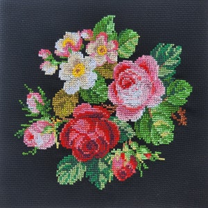 May include: A close-up of a cross-stitch embroidery featuring a bouquet of pink and red roses with white flowers and green leaves on a black background.