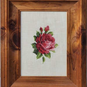 May include: A framed cross-stitch embroidery of a single red rose with green leaves and stems on a white linen background.