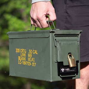 May include: An olive green metal ammo can with a black latch and a gold padlock. The can has a handle and text that reads "100 CRTG .50 CAL LINK M9 BLANK M1A1 LC-18H703-017". The latch has the text "LATCH LOCK AMMO CAN SECURITY".
