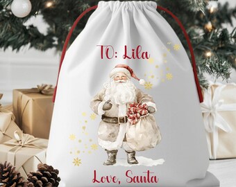 May include: White drawstring gift bag featuring a watercolor illustration of Santa Claus holding a sack of presents. The bag has red drawstrings and text that reads "To: Lila" and "Love, Santa" in red script, with gold snowflake accents.