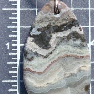 May include: A silver key chain with a light brown, white, and gray agate stone attached. The stone has a swirling pattern.