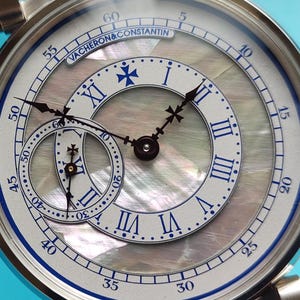Pode incluir: Close-up de um rel&oacute;gio de luxo com caixa prateada e mostrador em madrep&eacute;rola. O rel&oacute;gio apresenta algarismos romanos, detalhes azuis e um submostrador. A marca "VACHERON & CONSTANTIN" &eacute; vis&iacute;vel.