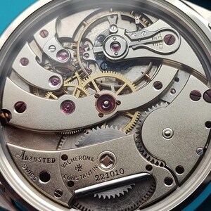 Pode incluir: Close-up do mecanismo de um rel&oacute;gio de pulso prateado com engrenagens intrincadas, joias e o texto "Adjusted Swiss Vacheron & Constantin 221010". Os componentes internos do rel&oacute;gio s&atilde;o vis&iacute;veis atrav&eacute;s de um cristal transparente.