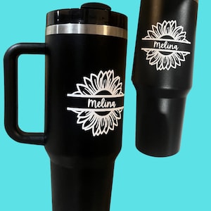 Puede incluir: Dos tazas de viaje de acero inoxidable negro con un diseño de girasol blanco y el nombre "Melina" impreso en cada taza.