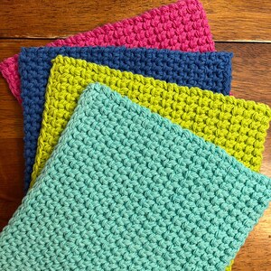 Könnte beinhalten: Vier gehäkelte Geschirrtücher in verschiedenen Farben: Türkis, Limettengrün, Blau und Pink. Die Geschirrtücher sind übereinander auf einer Holzoberfläche gestapelt.