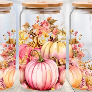 May include: Three clear glass tumblers with bamboo lids and glass straws, each featuring a wrap-around design of pink and orange pumpkins, autumn leaves, and swirling vines. The design is printed on the exterior of the cylindrical glass vessels.