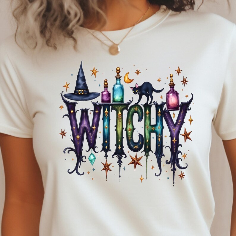 May include: A white t-shirt featuring a graphic print with the word WITCHY in large, ornate, gradient-coloured letters. The design includes a black witch hat, colourful potion bottles, a black cat, a crescent moon, and various gold stars.