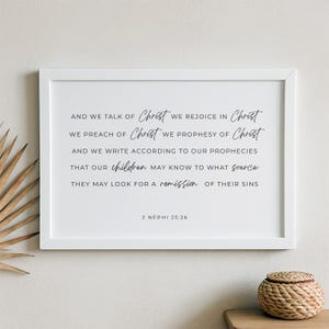 May include: A white framed wall art piece featuring black text that reads: AND WE TALK OF Christ WE REJOICE IN Christ WE PREACH OF Christ WE PROPHESY OF Christ AND WE WRITE ACCORDING TO OUR PROPHECIES THAT OUR children MAY KNOW TO WHAT source THEY MAY LOOK FOR A remission OF THEIR SINS 2 NEPHI 25:26.