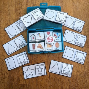 May include: A blue plastic storage box with a variety of white cards featuring different shapes, including a heart, circle, oval, triangle, square, pentagon, diamond, octagon, and star. The cards have the name of the shape printed on them.