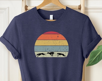 May include: A navy blue t-shirt with a vintage sunset graphic featuring three running dogs. The sunset is in shades of orange, yellow, and blue.