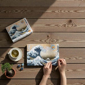 Peut inclure Un puzzle de 3000 pièces représentant une œuvre d'art japonaise célèbre, La Grande Vague de Kanagawa de Katsushika Hokusai. L'image représente une grande vague bleue qui se brise sur trois bateaux avec le mont Fuji en arrière-plan.