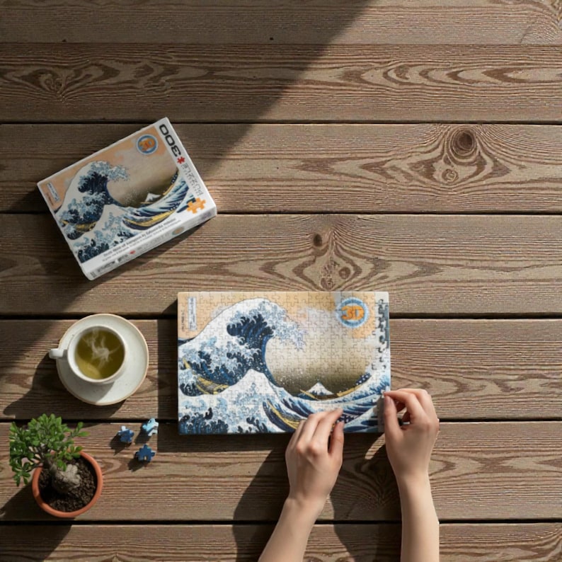 Peut inclure Un puzzle de 3000 pièces représentant une œuvre d'art japonaise célèbre, La Grande Vague de Kanagawa de Katsushika Hokusai. L'image représente une grande vague bleue qui se brise sur trois bateaux avec le mont Fuji en arrière-plan.