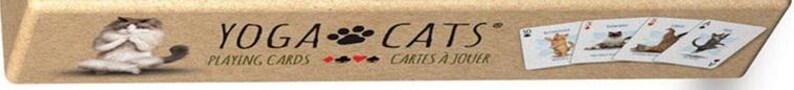 May include: A deck of playing cards with a brown background and the text "Yoga Cats" in black. The cards feature illustrations of cats in yoga poses. The text "Playing Cards" and "Cartes a Jouer" are also visible.