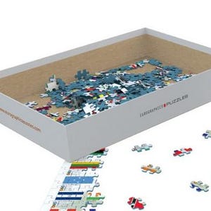 K&ouml;nnte beinhalten: Eine wei&szlig;e Box mit einem blauen Deckel ist ge&ouml;ffnet und mit einem Puzzle gef&uuml;llt. Die Box tr&auml;gt den Text "Eurographics Puzzles" und eine aufgedruckte Website-Adresse. Die Puzzleteile sind auf einer wei&szlig;en Oberfl&auml;che um die Box herum verstreut.