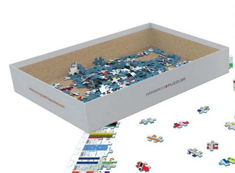 K&ouml;nnte beinhalten: Eine wei&szlig;e Box mit einem blauen Deckel ist ge&ouml;ffnet und mit einem Puzzle gef&uuml;llt. Die Box tr&auml;gt den Text "Eurographics Puzzles" und eine aufgedruckte Website-Adresse. Die Puzzleteile sind auf einer wei&szlig;en Oberfl&auml;che um die Box herum verstreut.