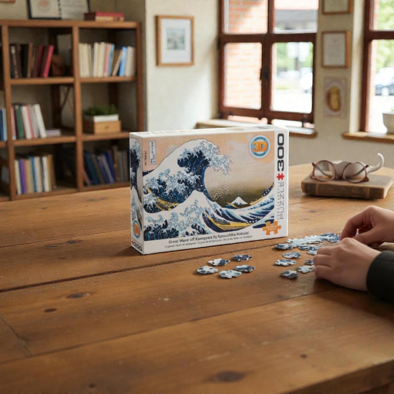 Peut inclure Un puzzle de 3000 pièces représentant une œuvre d'art japonaise célèbre, La Grande Vague de Kanagawa de Katsushika Hokusai. L'image représente une grande vague bleue qui se brise sur trois bateaux avec le mont Fuji en arrière-plan.