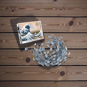 Peut inclure Un puzzle de 3000 pièces représentant une œuvre d'art japonaise célèbre, La Grande Vague de Kanagawa de Katsushika Hokusai. L'image représente une grande vague bleue qui se brise sur trois bateaux avec le mont Fuji en arrière-plan.
