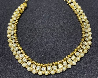 May include: A gold and white necklace with a layered design of small pearls and rhinestones.